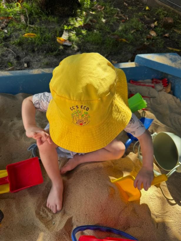 Criança de chapéu amarelo brincando na caixa de areia do quintal