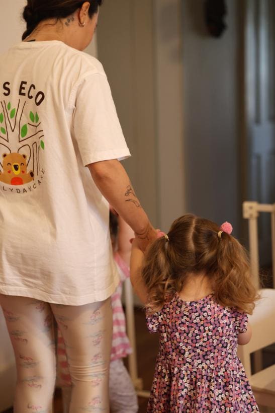 Educadora caminhando de mãos dadas com uma criança pequena dentro de casa
