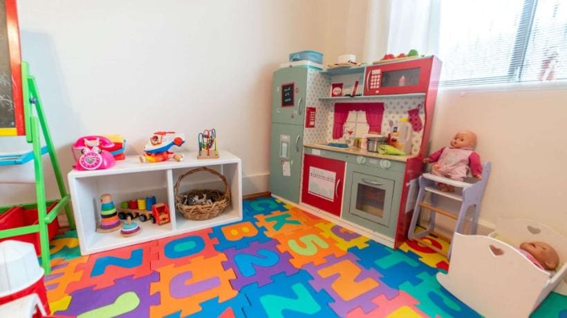 Sala de brincar do Family Day Care, com cozinha de brinquedo e tapete de letras