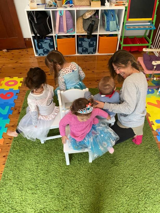 Educadora brincando no chão com um grupo de crianças fantasiadas na sala de atividades